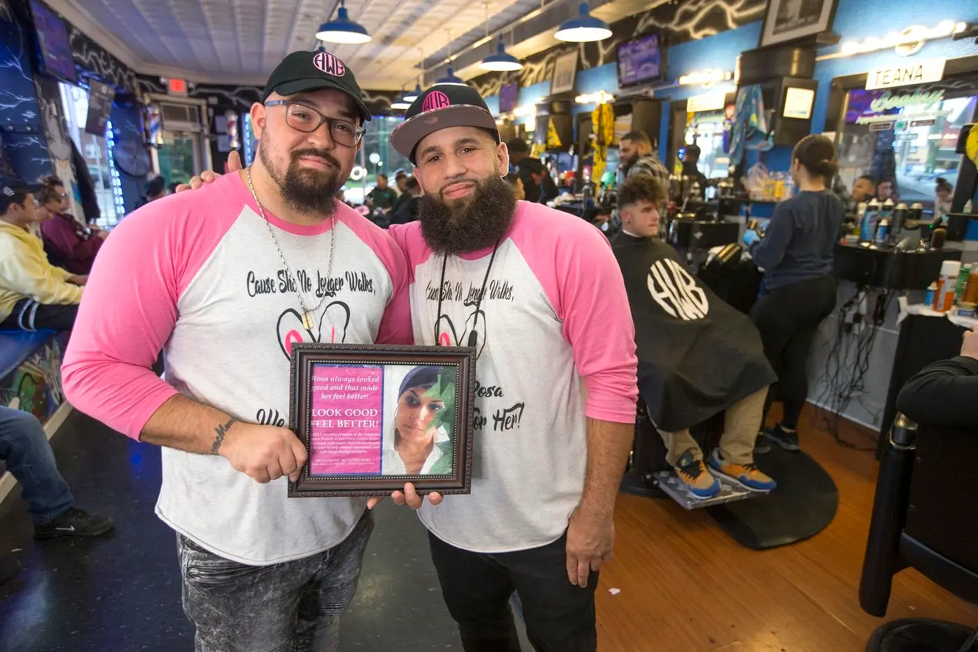 Two Hair Wizards barbers in matching tribute shirts holding a framed photo of Rosa in the shop