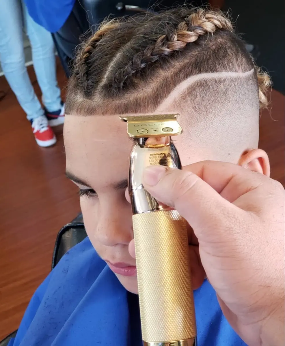 A barber gently detailing a braided style and fade on a young boy
